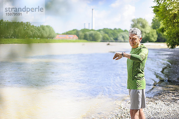 Aktiver älterer Mann prüft die Zeit  während er an einem sonnigen Tag am Flussufer steht