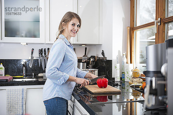 Lächelnde schöne Frau schneidet rote Paprika an der Küchentheke