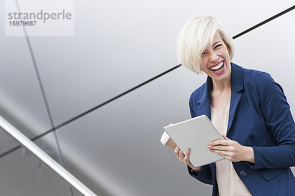 Porträt einer lachenden blonden Geschäftsfrau mit Tablet und Kaffee zum Mitnehmen