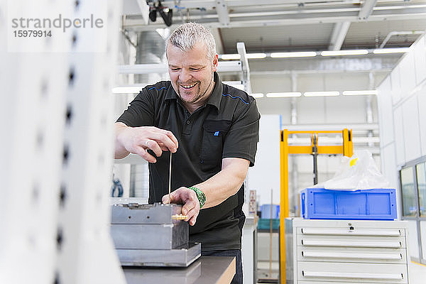 Lächelnder Mann bei der Arbeit an einer Werkbank in einer Fabrik