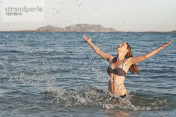 Glückliche Frau im Bikini steht im Meer und spritzt mit Wasser  Sardinien  Italien