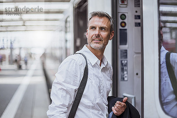 Geschäftsmann schaut beim Einsteigen in einen Zug am Bahnsteig weg