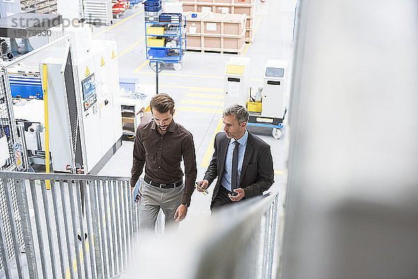 Zwei Geschäftsleute gehen eine Treppe in einer Fabrik hinauf
