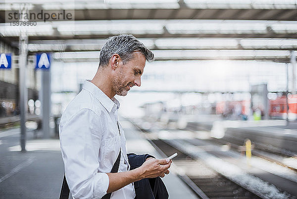 Geschäftsmann  der ein Smartphone benutzt  während er am Bahnsteig steht