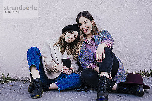 Porträt von zwei glücklichen Frauen  die zusammen auf dem Bürgersteig sitzen