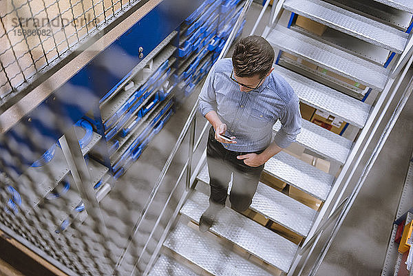 Geschäftsmann mit Smartphone beim Treppensteigen in einer Fabrik