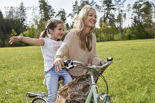 Mädchen mit ausgestreckten Armen genießt Fahrradfahrt mit Mutter auf Pflanzen