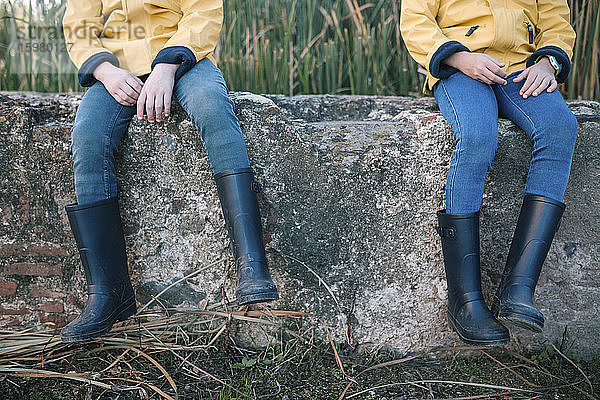 Gummistiefel von Geschwistern  die auf einer Stützmauer sitzen