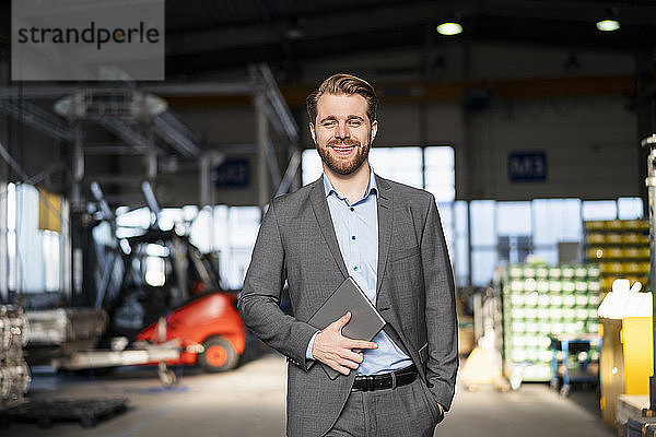 Porträt eines lächelnden jungen Geschäftsmannes mit Tablet in einer Fabrik