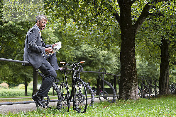 Geschäftsmann liest Zeitung und sitzt auf einem Geländer in einem öffentlichen Park