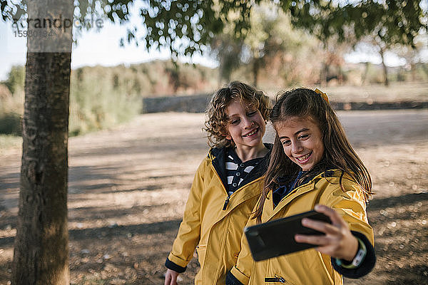 Lächelndes Mädchen nimmt Selfie mit Bruder von Smartphone im Freien