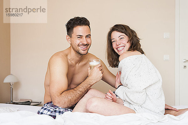 Glückliches junges Paar sitzt zu Hause auf dem Bett