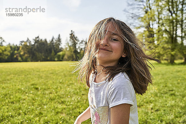 Verspieltes Mädchen mit zerzaustem Haar im Gras stehend an einem sonnigen Tag