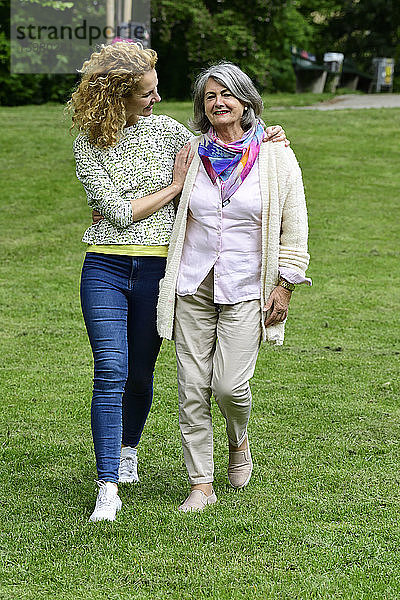 Lächelnde ältere Frau  die mit ihrer Tochter auf einer Wiese im Park spazieren geht