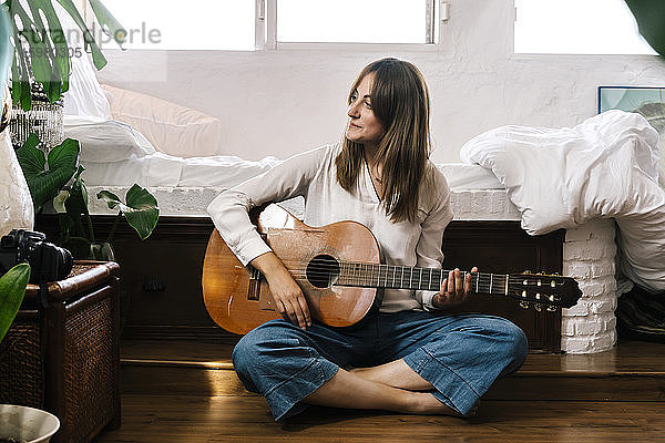 Frau sitzt auf dem Boden vor dem Bett mit Gitarre
