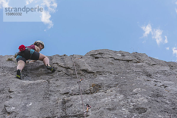 Junge Frau klettert auf einen Felsen und blickt in den Himmel