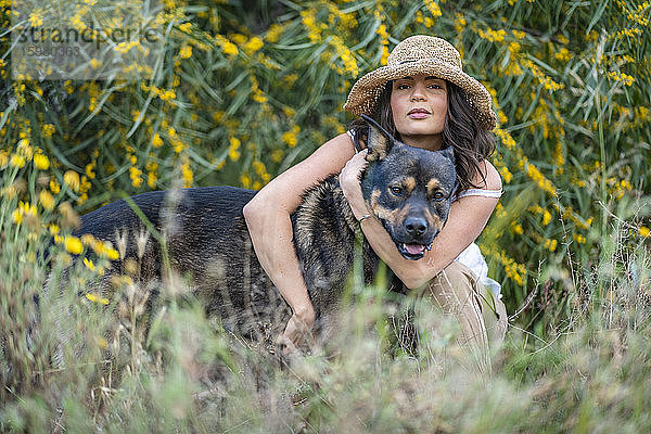 Porträt einer schönen jungen Frau  die einen Hund umarmt  während sie inmitten von Pflanzen hockt  Alicante  Provinz Alicante  Spanien