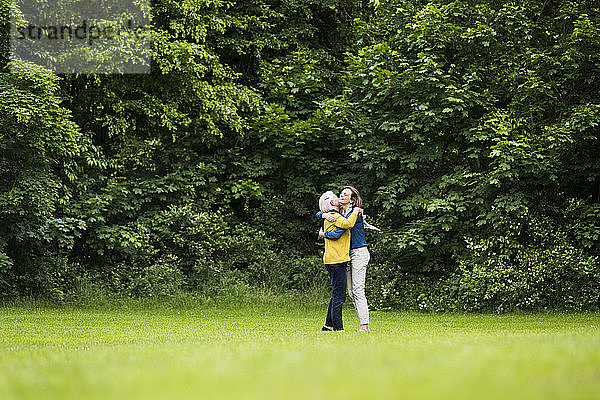 Ältere Frau und erwachsene Tochter umarmen sich in einem Park