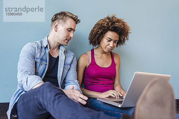 Junge Frau und Mann sitzen in einem modernen Büro auf dem Boden und benutzen einen Laptop