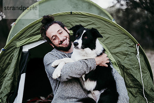 Glücklicher Mann  der seinen Hund in einem Zelt umarmt