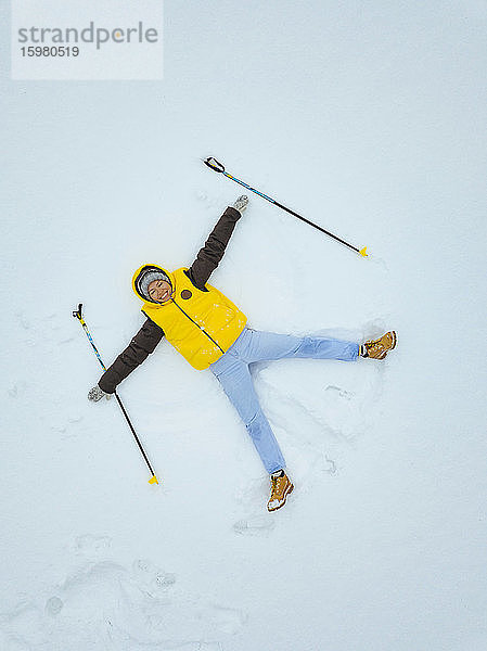 Russland  Luftaufnahme einer erwachsenen Frau  die mit Skistöcken in den Händen einen Schneeengel macht