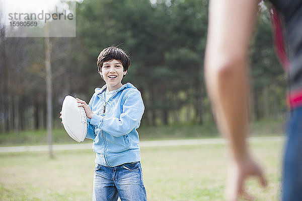 Glücklicher Junge spielt Rugby mit seinem Vater im Park