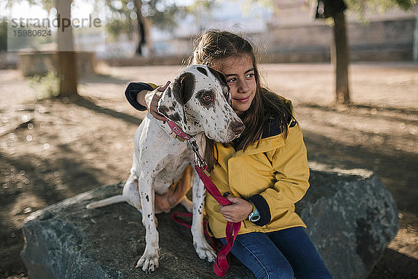 Niedliches Mädchen umarmt Hund und sitzt auf einem Felsen
