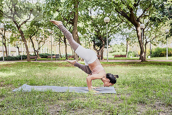Mittlere erwachsene Frau übt Yoga auf Matte im Park  Krähenstellung