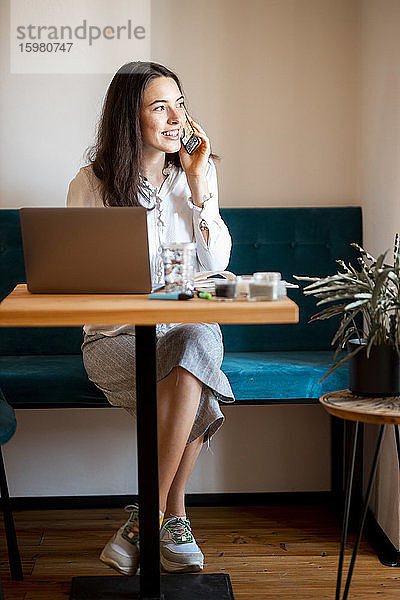 Porträt einer lächelnden jungen Frau am Telefon bei der Arbeit im Heimbüro