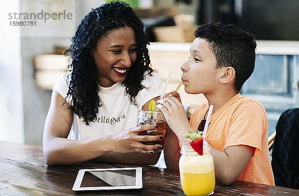 Lächelnde Frau  die ihr Getränk mit ihrem Sohn im Restaurant teilt