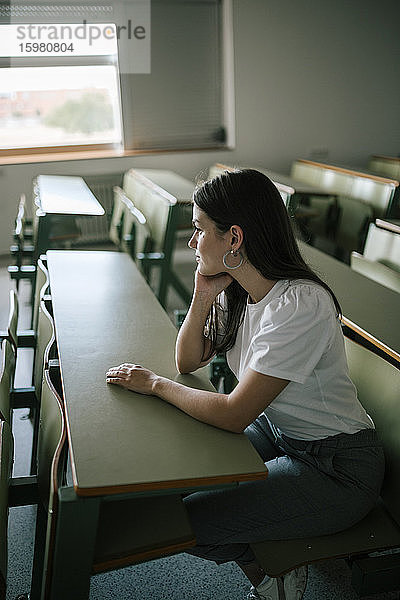 Seitenansicht einer nachdenklichen jungen Frau  die am Schreibtisch sitzt und wegschaut