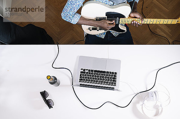 Junger Mann übt Gitarre  während er von einem Online-Tutorial zu Hause lernt