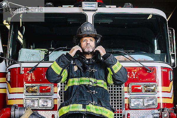 USA  New York  Porträt eines Feuerwehrmanns  der seinen Helm vor einem Feuerwehrauto aufsetzt