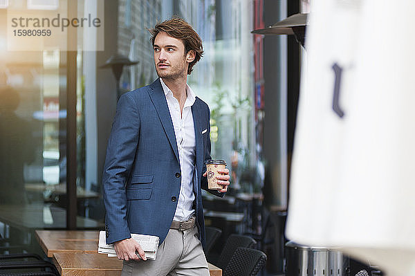 Porträt eines jungen Geschäftsmannes mit Zeitung und Kaffee zum Mitnehmen im Freien