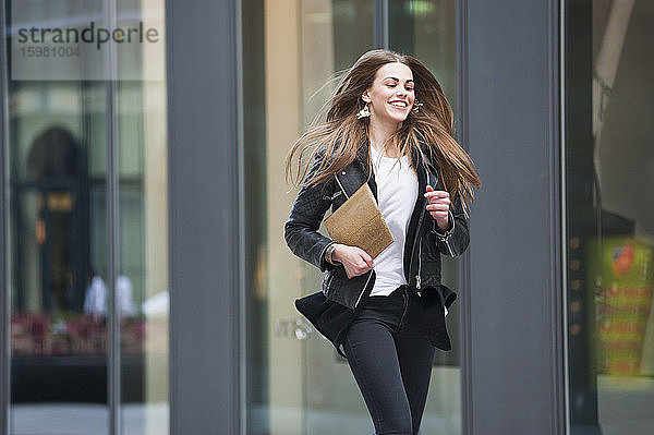 Fröhliche junge Frau mit Laptop beim Laufen in der Stadt