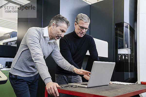 Männliche Vorgesetzte diskutieren in einer Fabrik über einen Laptop