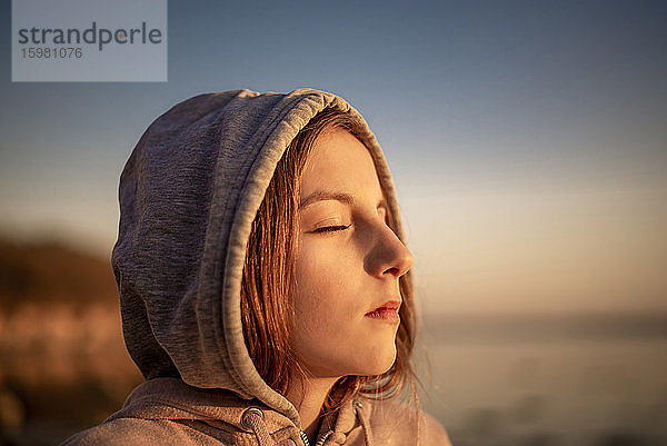 Deutschland  Mecklenburg-Vorpommern  Insel Poel  Nahaufnahme eines jungen Mädchens mit geschlossenen Augen am Strand bei Sonnenuntergang