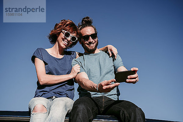 Glückliches Paar  das auf dem Dach eines Minivans sitzt und ein Selfie macht