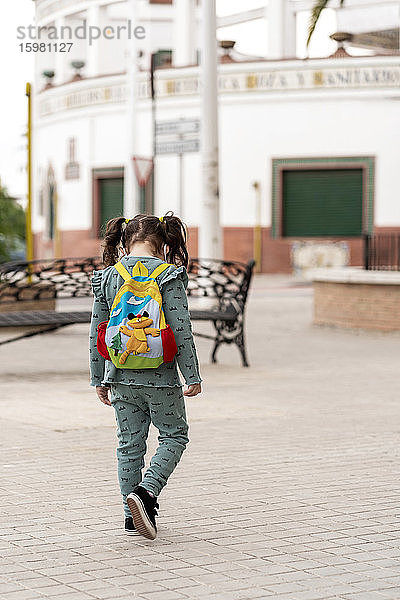 Rückansicht eines Mädchens mit Rucksack und Maske auf dem Platz