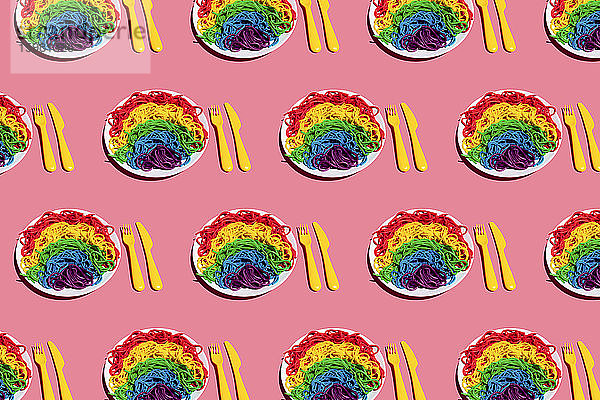Muster von Tellern mit regenbogenfarbenen Spaghetti vor rosa Hintergrund