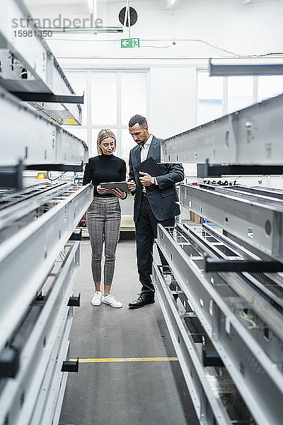 Geschäftsmann und Frau mit Tablet an Metallstäben in einer Fabrikhalle