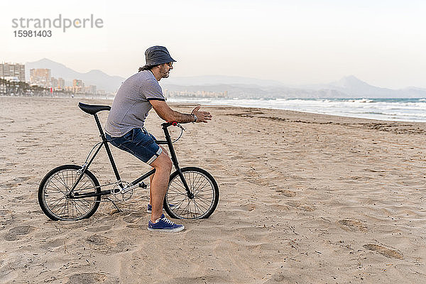 Älterer Mann mit Fahrrad  der am Strand sitzt und das Meer beobachtet