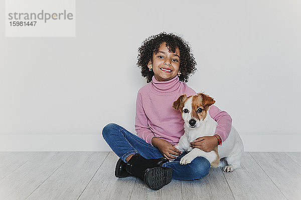 Porträt eines lächelnden kleinen Mädchens  das mit seinem Hund auf dem Boden sitzt
