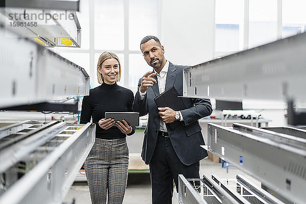 Geschäftsmann und Frau mit Tablet an Metallstäben in einer Fabrikhalle