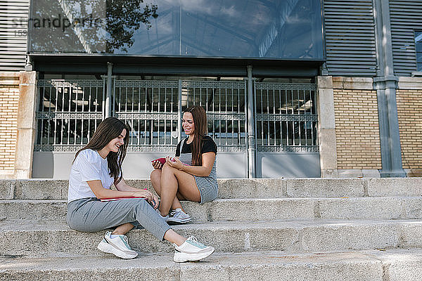 Lächelnde junge Studentinnen in voller Länge  die sich auf einer Treppe auf dem Campus einer Universität unterhalten
