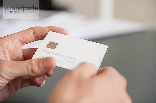 Hände eines mittleren erwachsenen Mannes  der eine leere weiße Kreditkarte hält