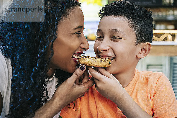 Nahaufnahme einer fröhlichen Mutter und eines Sohnes  die sich einen Keks teilen  während sie im Restaurant sitzen