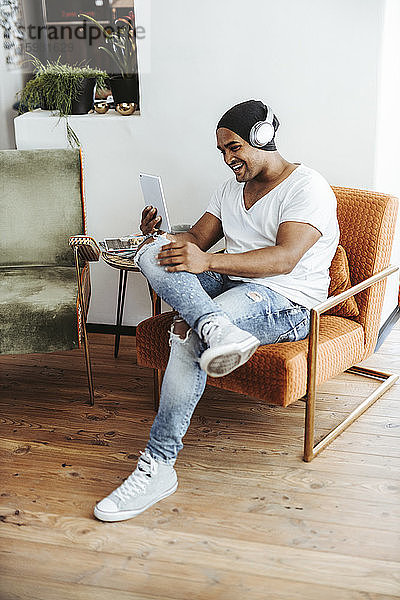 Lachender Mann mit Mini-Tablet und Kopfhörern zu Hause