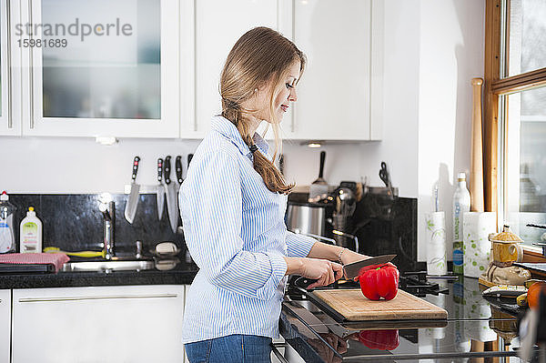 Junge Frau schneidet rote Paprika am Küchentisch