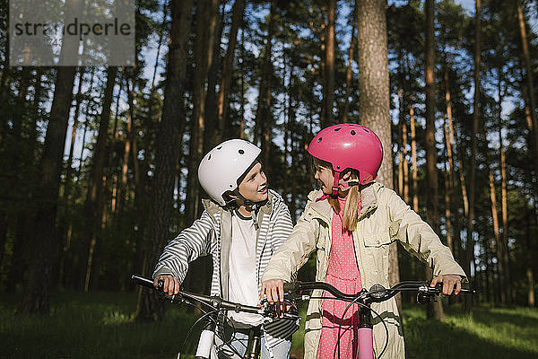 Mädchen und Junge unterhalten sich beim Fahrradfahren im Wald